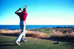 Red-shirted golfer completing a swing, looking away at his drive
