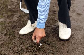 Golfer lifts his ball from mud