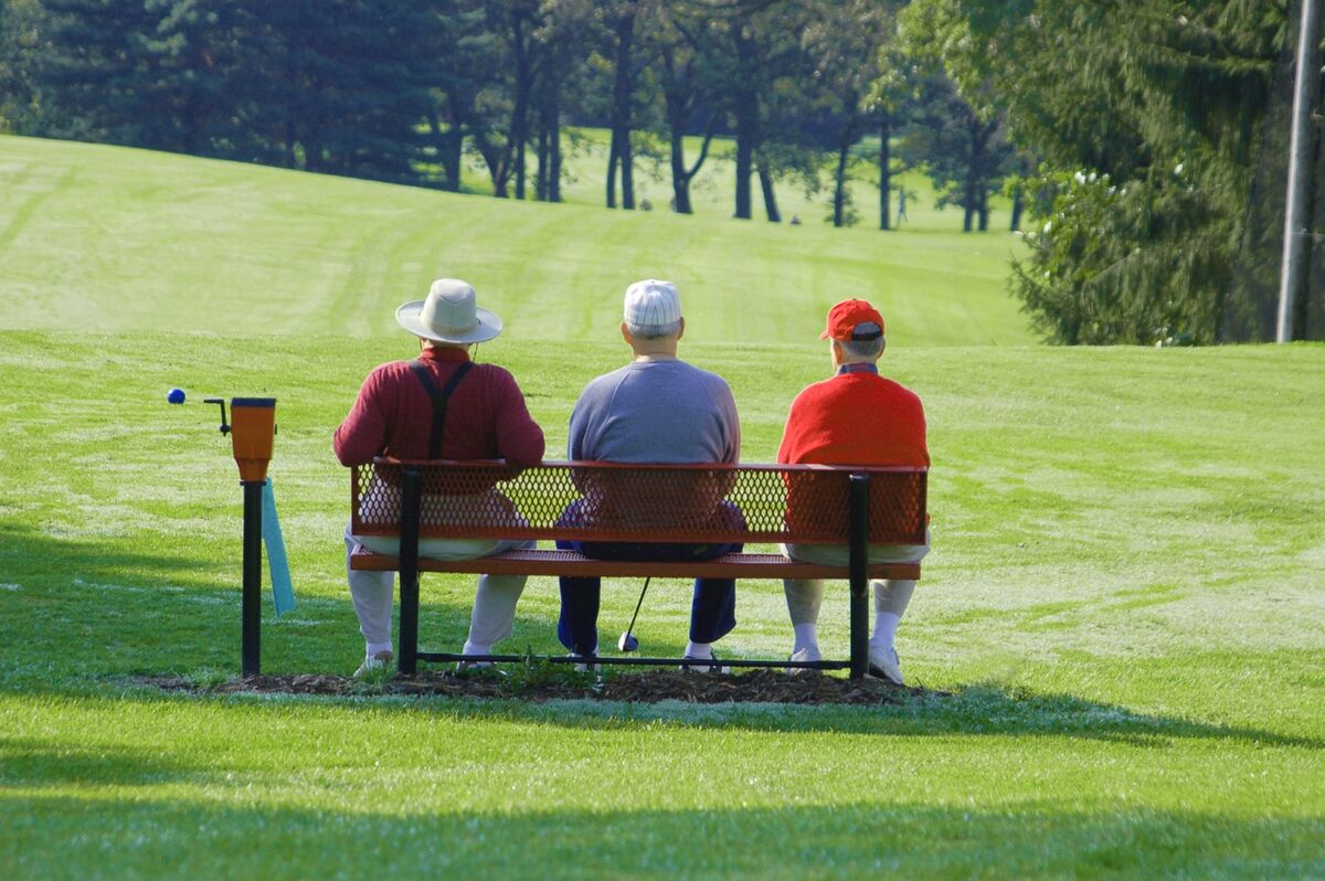 Three golfers wait on a bench