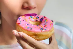 woman eating doughnut with pink icing