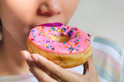 woman eating doughnut with pink icing