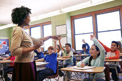 Group of children raising their hands to answer their teacher's question