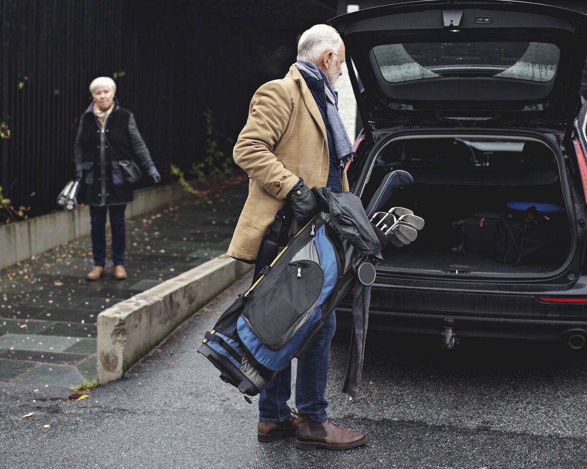 man loads golf clubs into car for a vacation