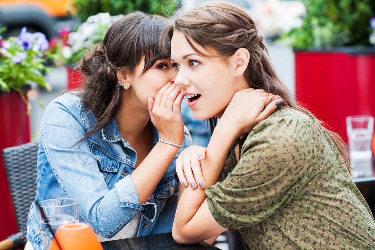 Two best friends sitting in a cafe whispering and gossiping