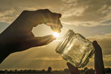 Person holding jar against sunny sky