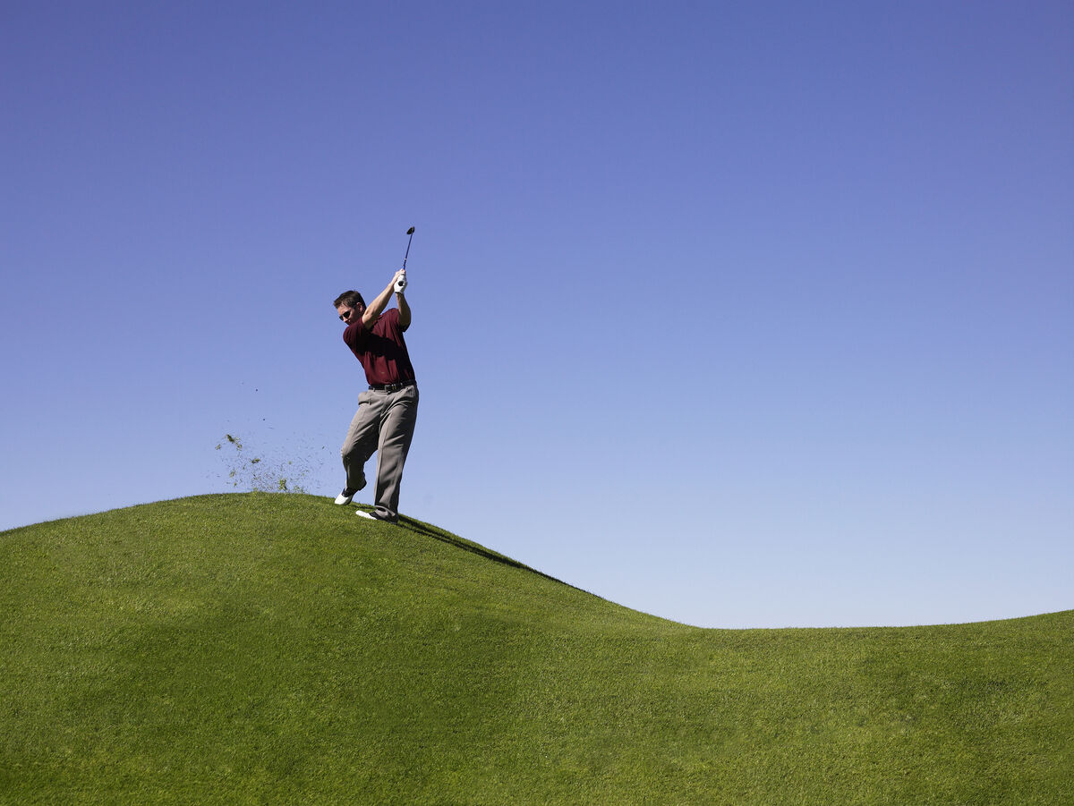 Male golfer hitting from a downhill lie