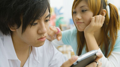 Teenage boy playing video game while girl pesters him