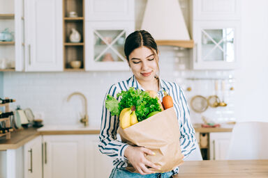 Woman holding eco shopping bag with fresh vegetables in modern kitchen