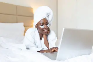 Woman with face cream lying on bed in bathrobe and towel on the head using a laptop