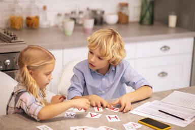 Two kids playing with cards with letters on the table