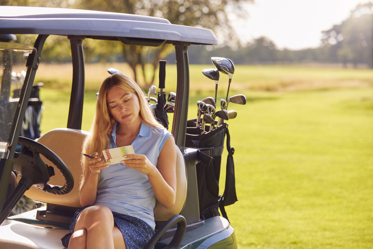 Woman studying the scorecard from her golf cart