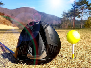A modern driver rests next to a teed up golf ball
