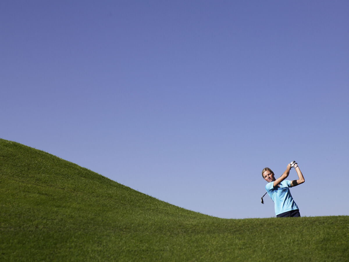 Golfer hitting the ball off a hill above her feet