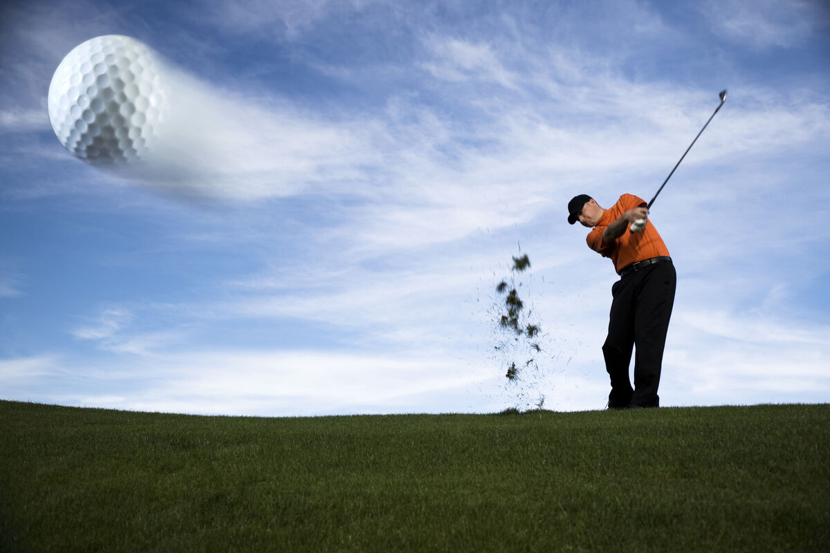 Golf ball mid-flight with golfer in follow through