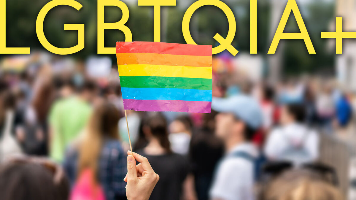 LGBTQIA+ abbreviation and flag with blurred crowd