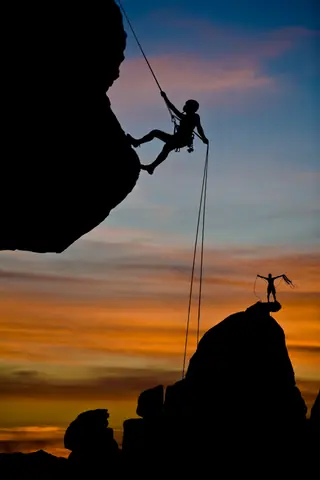 Person using ropes to rock climb as examples of courage