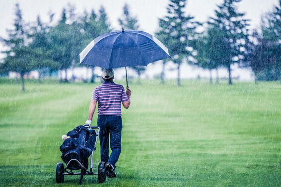 Golfer with umbrella in rain