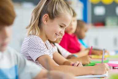 Girl sitting with other children in classroom and writing
