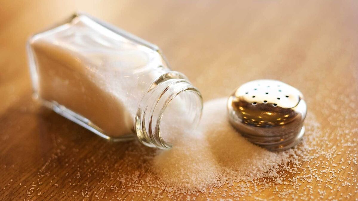 open salt shaker lying on table with salt spilling out