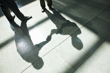 A shadow on a tiled floor of two businessmen shaking hands