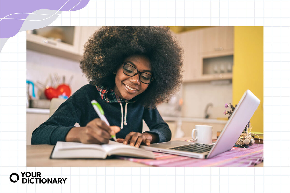 Woman Writing a Thesis Statement in Notebook Next To Laptop