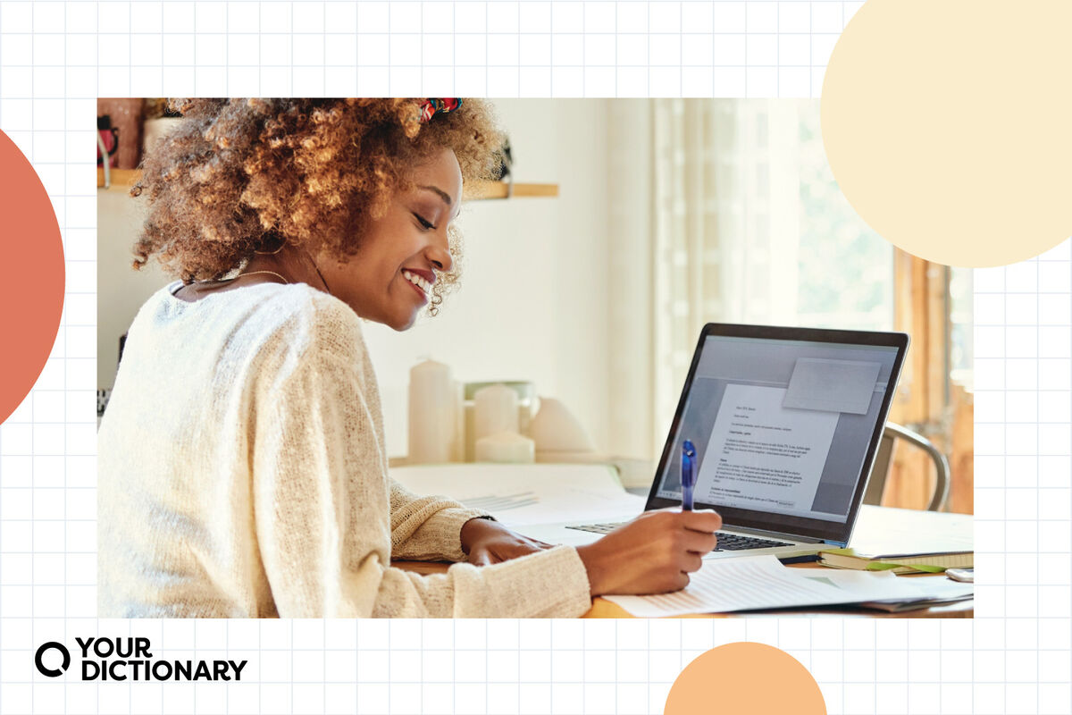 Woman Writing Introduction Paragraph in Notebook next to Laptop