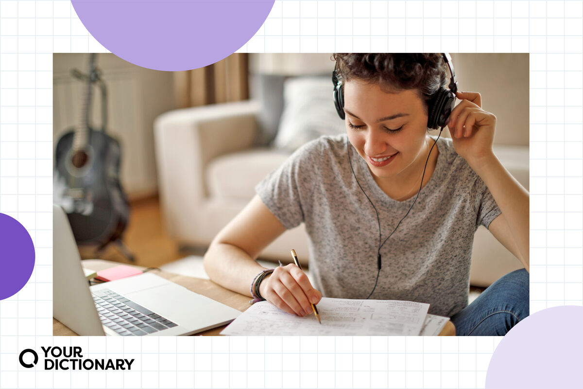 student with headphones writing essay outline on paper