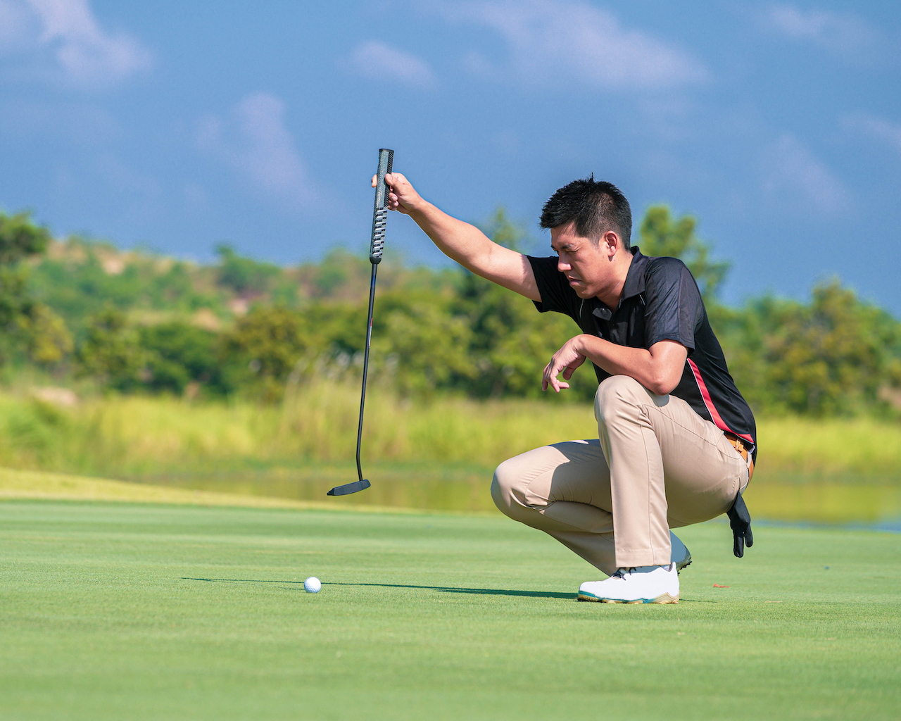 Man examining putting green with putter