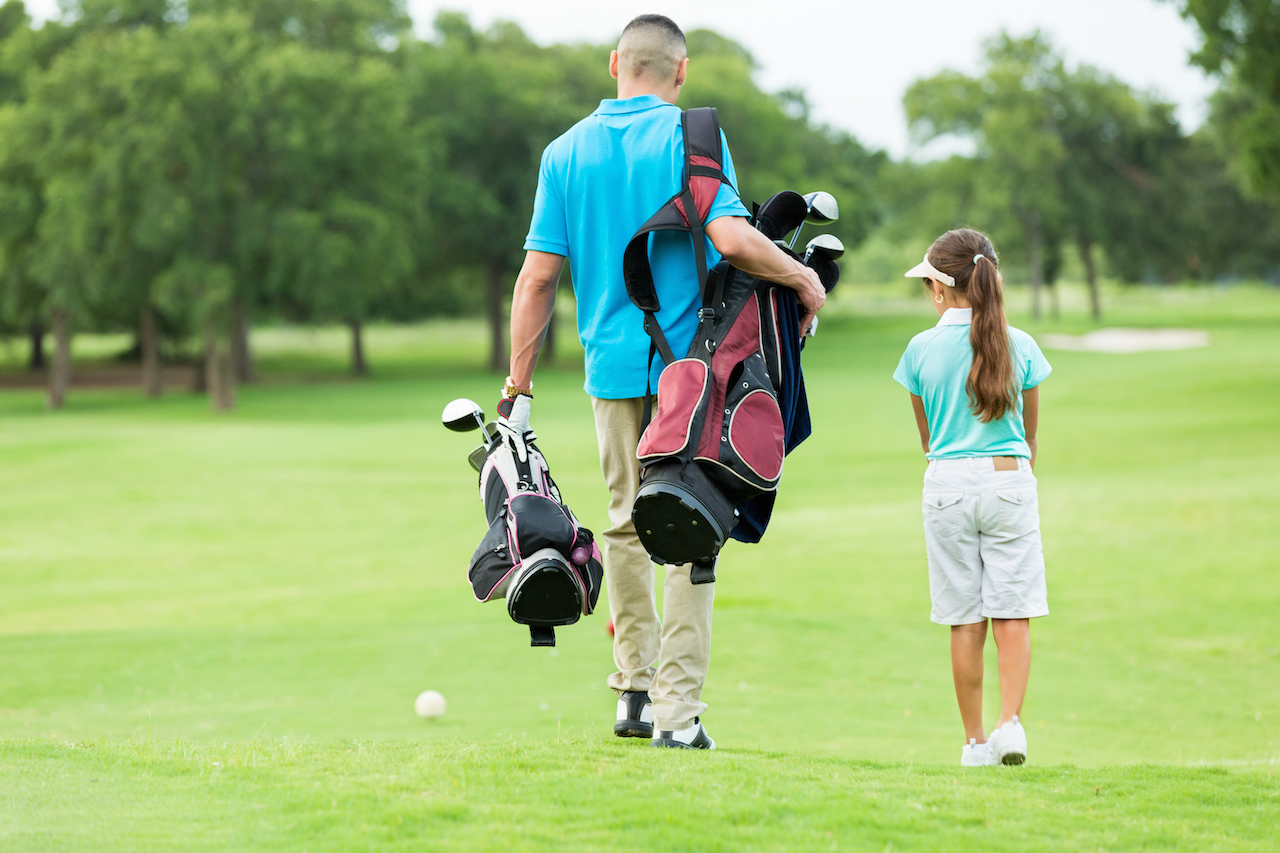 Man and child carrying golf clubs on course